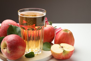 Photo of Fresh cider in glass and apples on white table, closeup