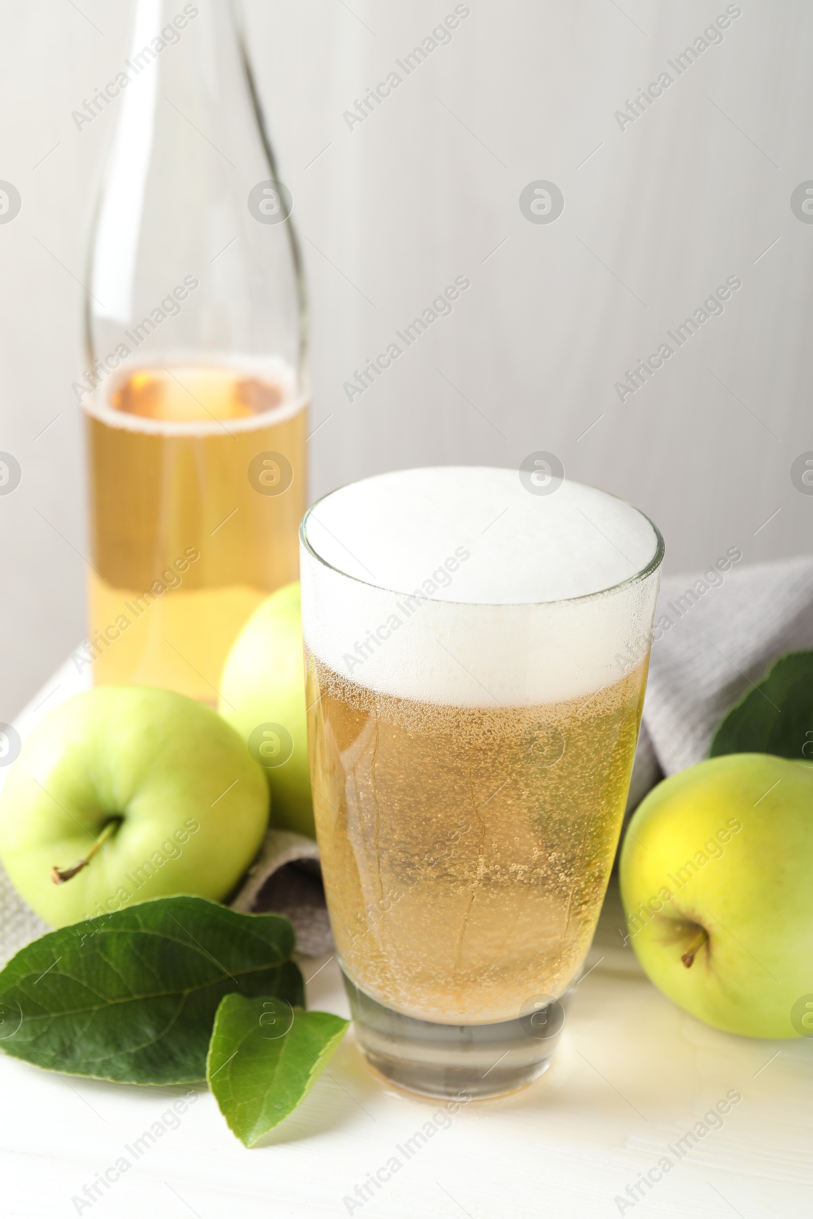 Fresh cider in glass, bottle and apples on white wooden table, closeup Photo of Fresh cider in glass, bottle and apples on white wooden table, closeup