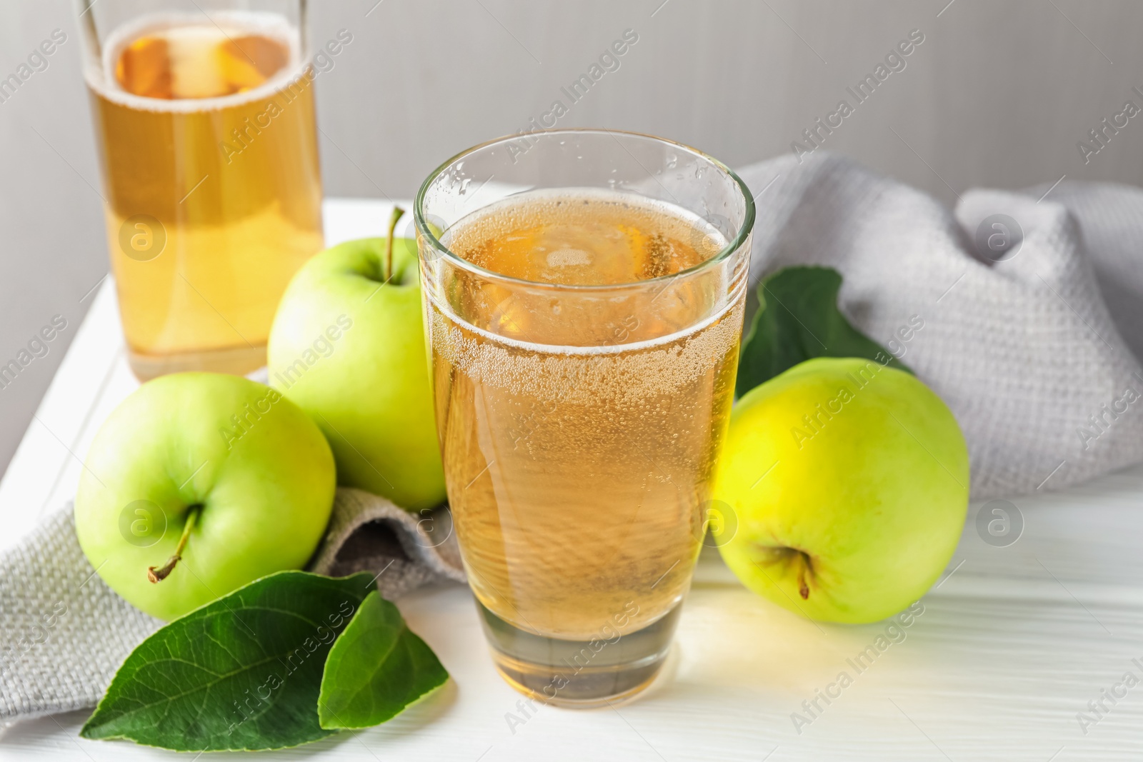 Fresh cider in glass, bottle and apples on white wooden table, closeup Photo of Fresh cider in glass, bottle and apples on white wooden table, closeup