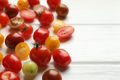 Photo of Different ripe tomatoes on white wooden table, closeup. Space for text
