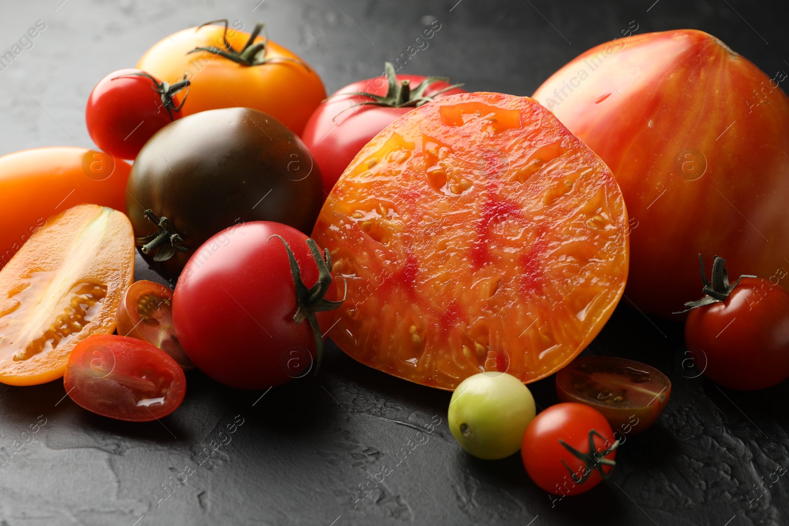 Photo of Different ripe tomatoes on black table, closeup