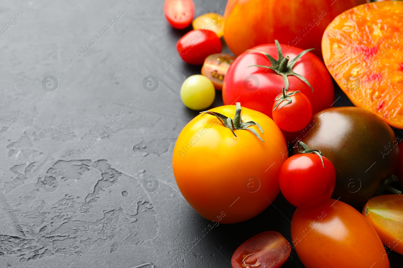 Photo of Different ripe tomatoes on black table, closeup. Space for text