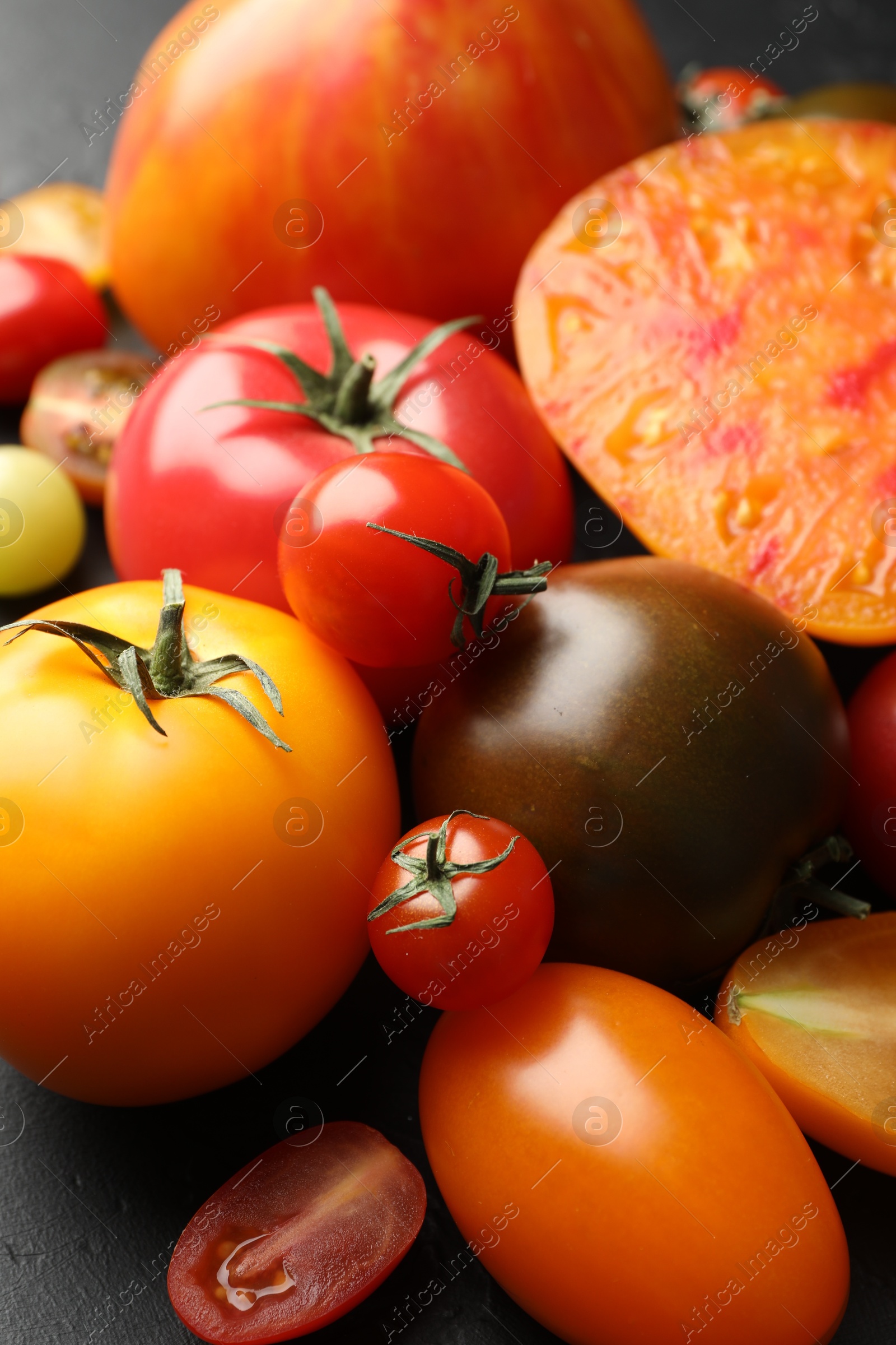 Photo of Different ripe tomatoes on black table, closeup