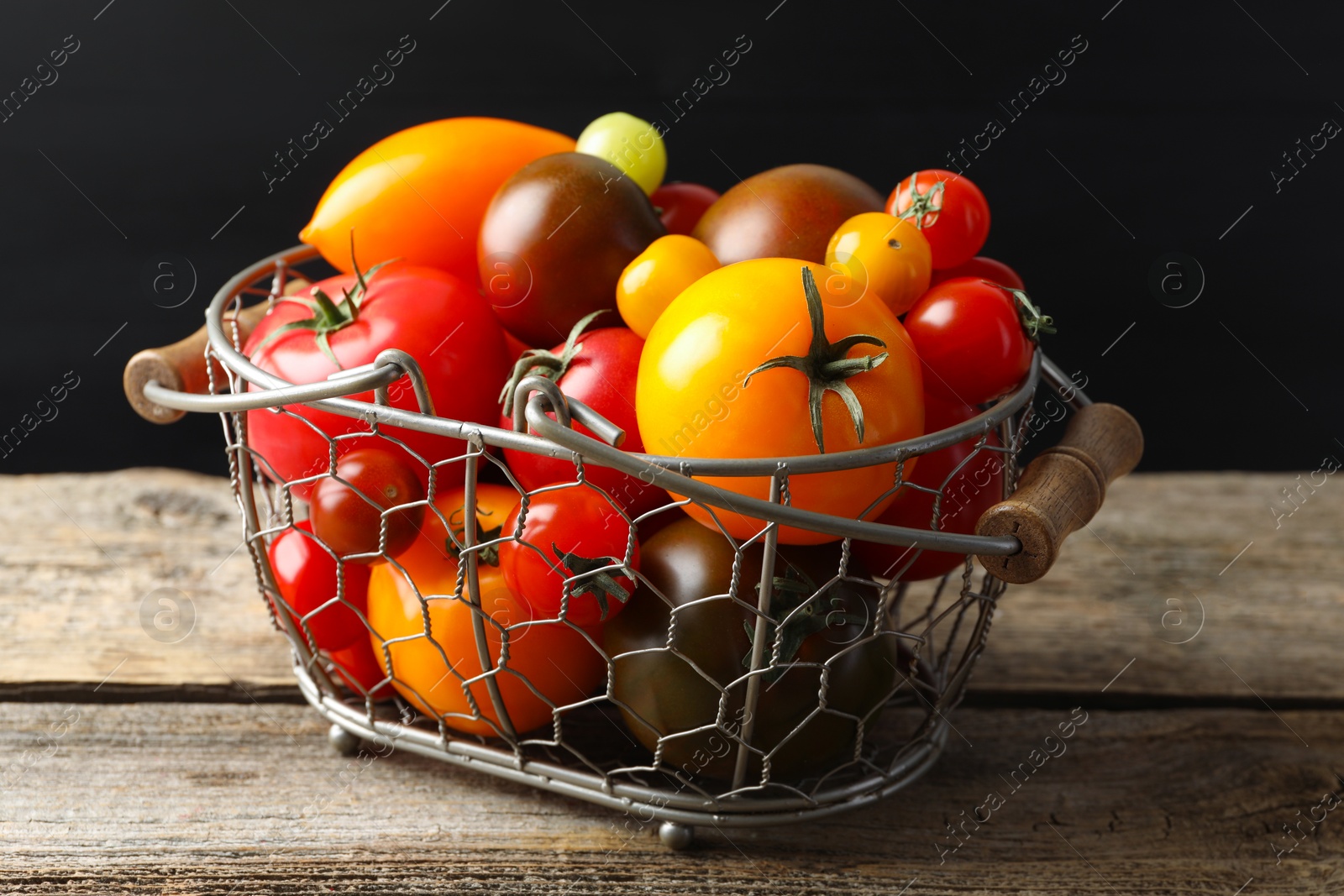Photo of Different ripe tomatoes in basket on wooden table, closeup