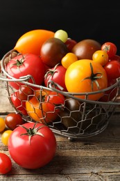 Photo of Different ripe tomatoes in basket on wooden table, closeup