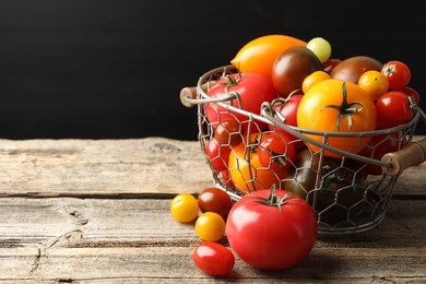 Photo of Different ripe tomatoes in basket on wooden table. Space for text