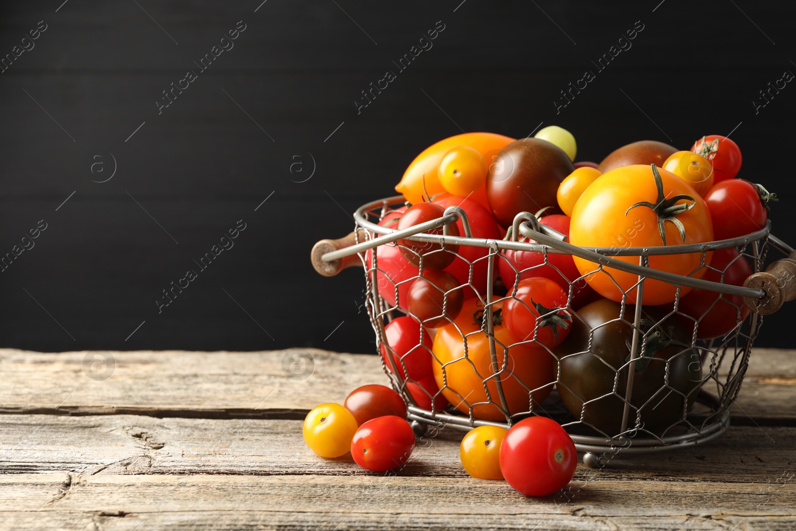 Photo of Different ripe tomatoes in basket on wooden table. Space for text