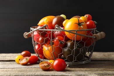 Photo of Different ripe tomatoes in basket on wooden table, closeup