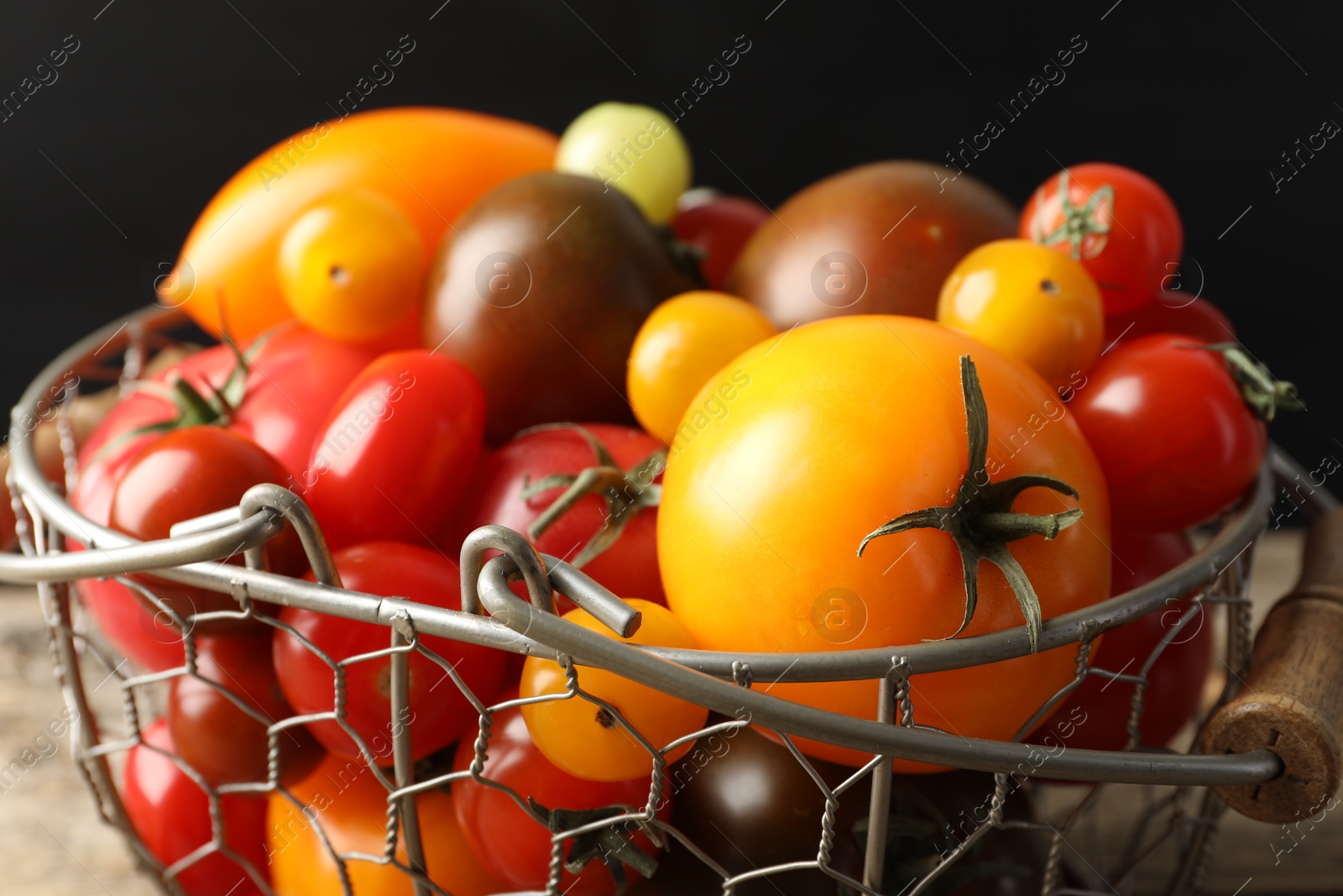 Photo of Different ripe tomatoes in basket on wooden table, closeup