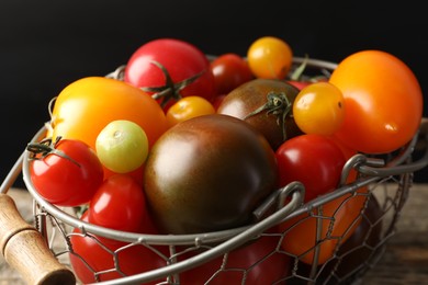 Photo of Different ripe tomatoes in basket on wooden table, closeup