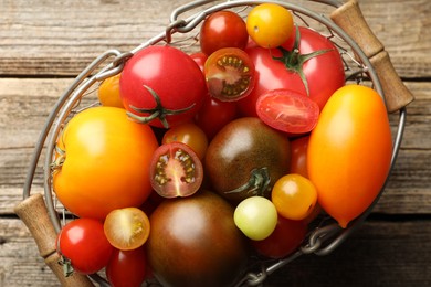 Photo of Different ripe tomatoes in basket on wooden table, top view