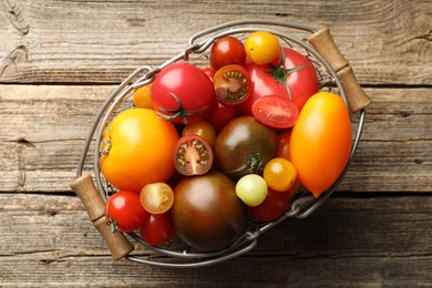 Photo of Different ripe tomatoes in basket on wooden table, top view