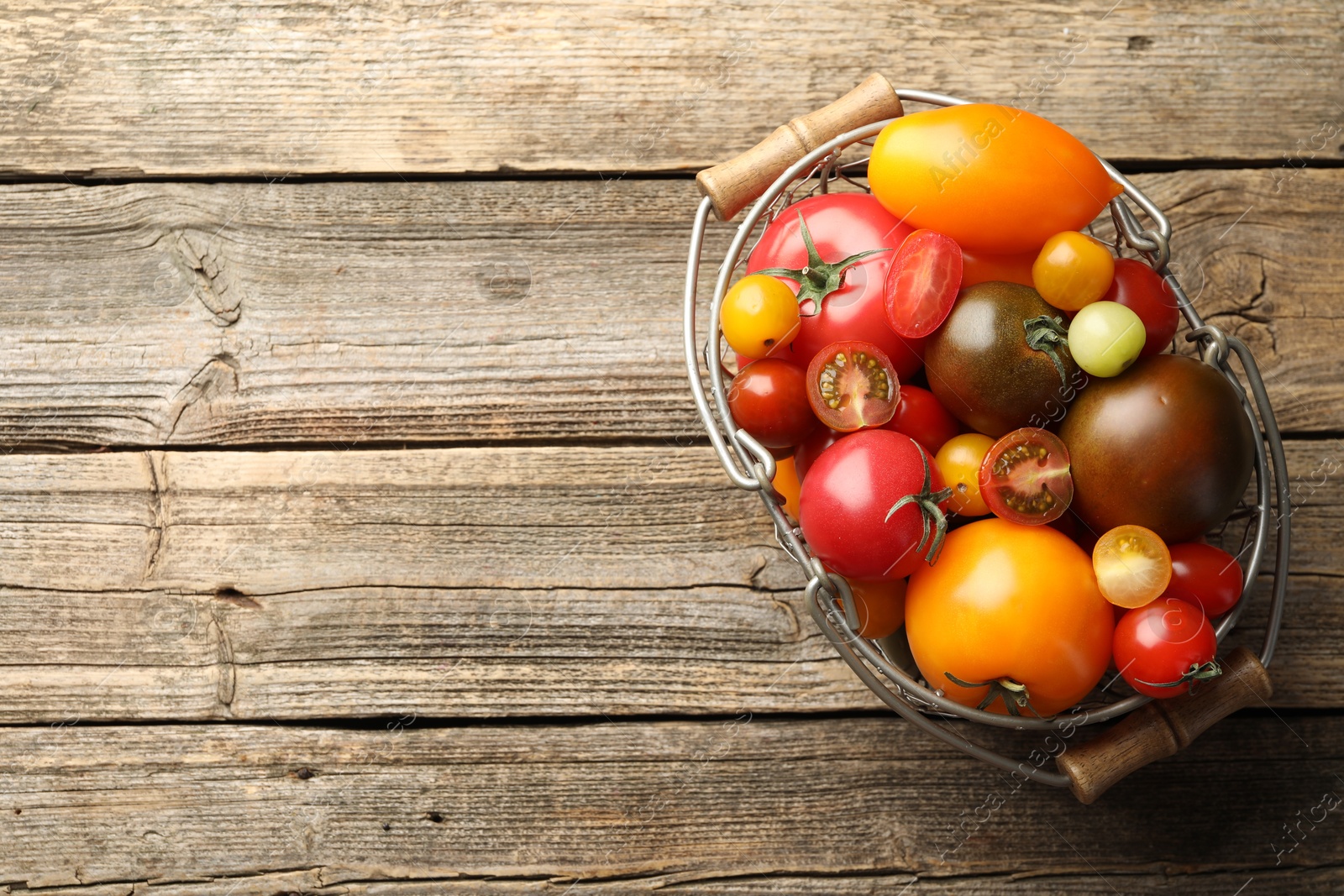 Photo of Different ripe tomatoes in basket on wooden table, top view. Space for text
