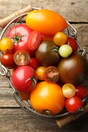 Photo of Different ripe tomatoes in basket on wooden table, top view