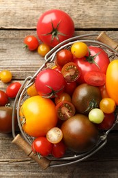 Photo of Different ripe tomatoes in basket on wooden table, top view