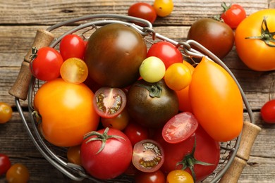 Photo of Different ripe tomatoes in basket on wooden table, top view