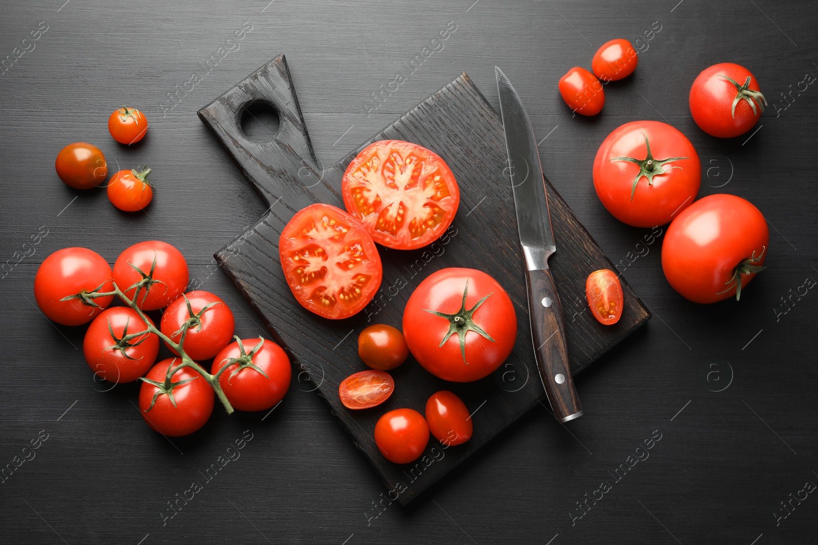 Photo of Whole and cut red tomatoes with knife on black table, flat lay