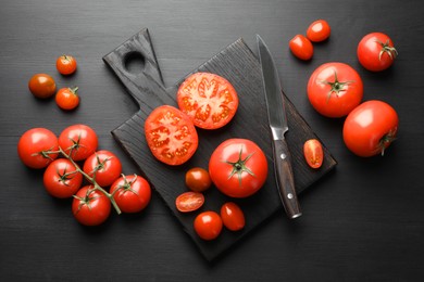 Photo of Whole and cut red tomatoes with knife on black table, flat lay