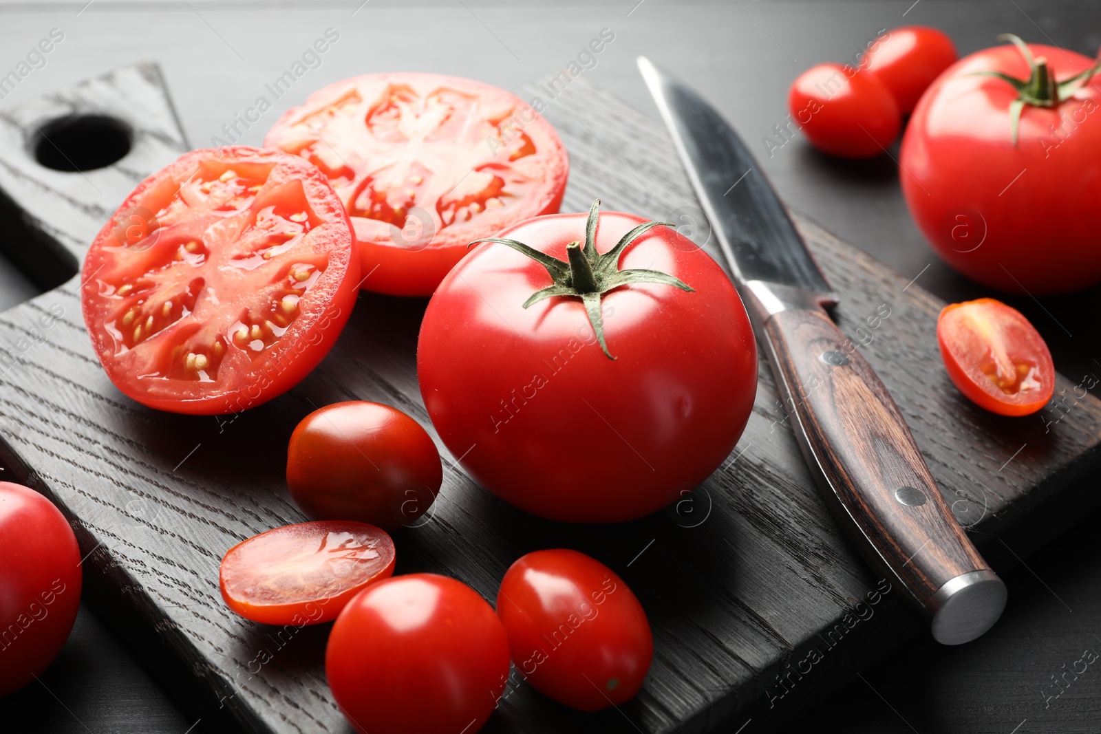 Photo of Whole and cut red tomatoes with knife on black table, closeup