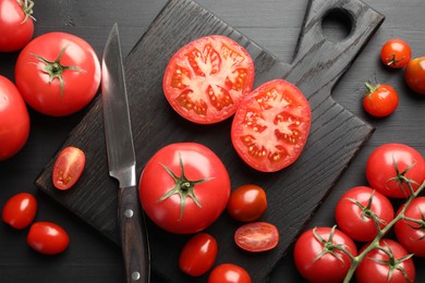Photo of Whole and cut red tomatoes with knife on black table, flat lay
