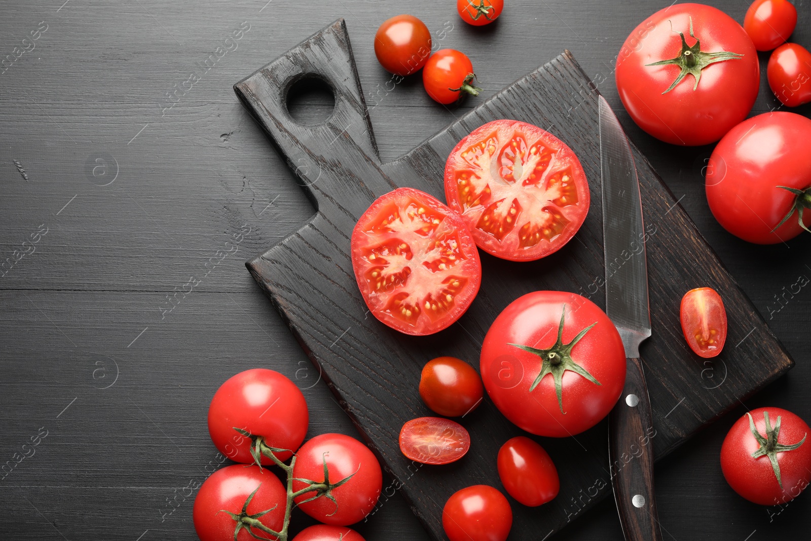 Photo of Whole and cut red tomatoes with knife on black table, flat lay