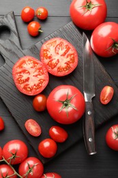 Photo of Whole and cut red tomatoes with knife on black table, flat lay