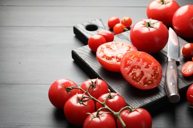 Photo of Whole and cut red tomatoes with knife on black table, closeup. Space for text
