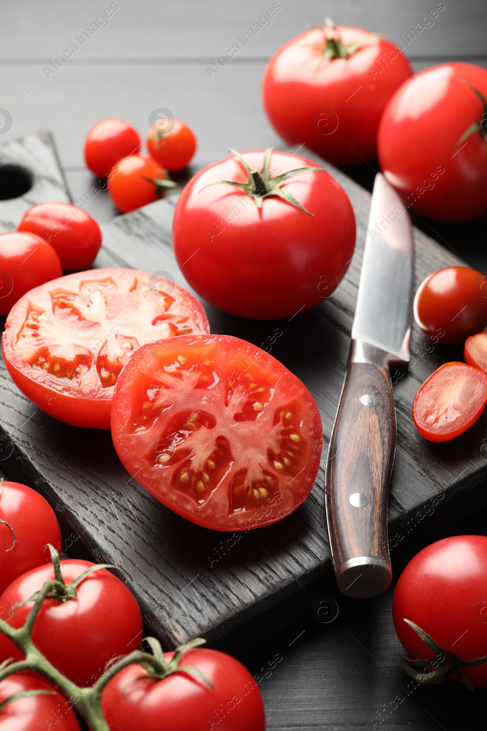 Whole and cut red tomatoes with knife on black table, closeup Photo of Whole and cut red tomatoes with knife on black table, closeup