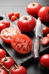 Photo of Whole and cut red tomatoes with knife on black table, closeup