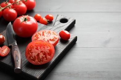 Photo of Whole and cut red tomatoes with knife on black table, closeup. Space for text