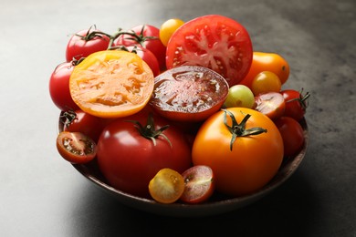 Photo of Different ripe tomatoes in bowl on grey table, closeup