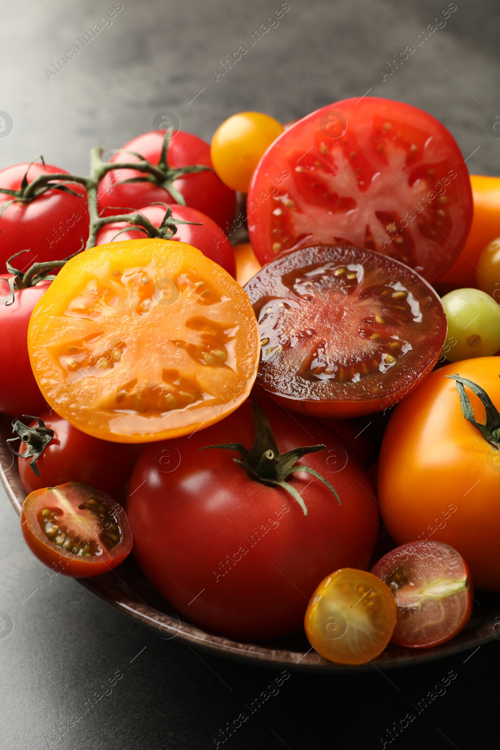 Photo of Different ripe tomatoes in bowl on grey table, closeup