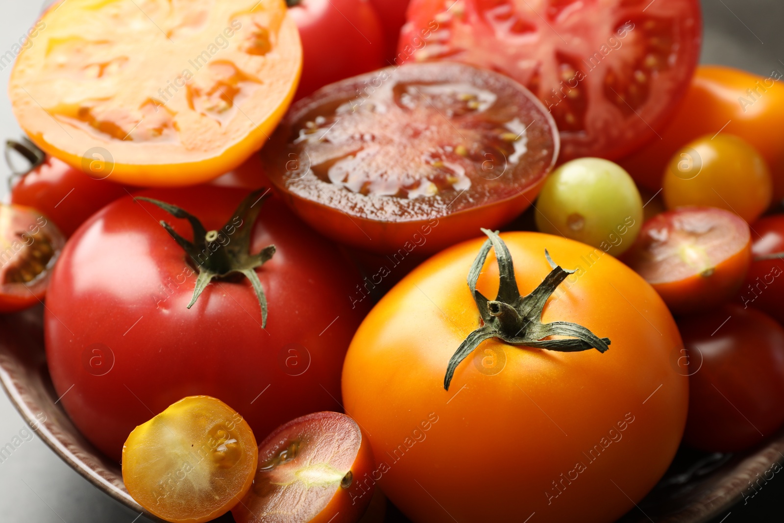 Photo of Different ripe tomatoes in bowl on grey table, closeup