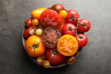 Photo of Different ripe tomatoes in bowl on grey table, top view