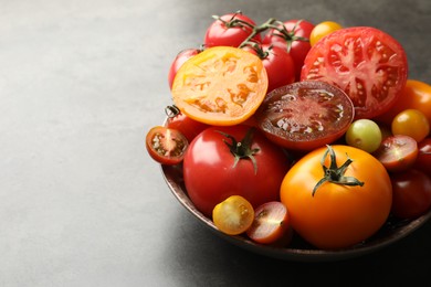 Photo of Different ripe tomatoes in bowl on grey table, closeup. Space for text