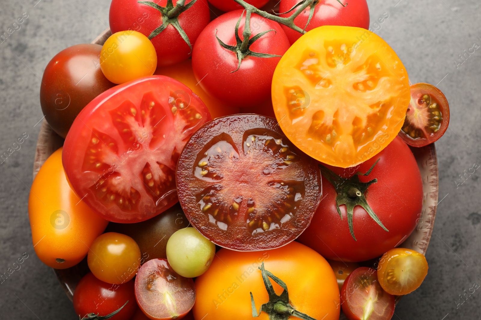 Different ripe tomatoes in bowl on grey table, top view Photo of Different ripe tomatoes in bowl on grey table, top view