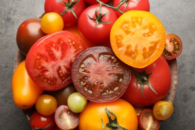 Photo of Different ripe tomatoes in bowl on grey table, top view