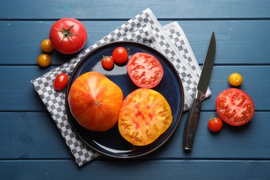 Photo of Different ripe tomatoes and knife on blue wooden table, flat lay