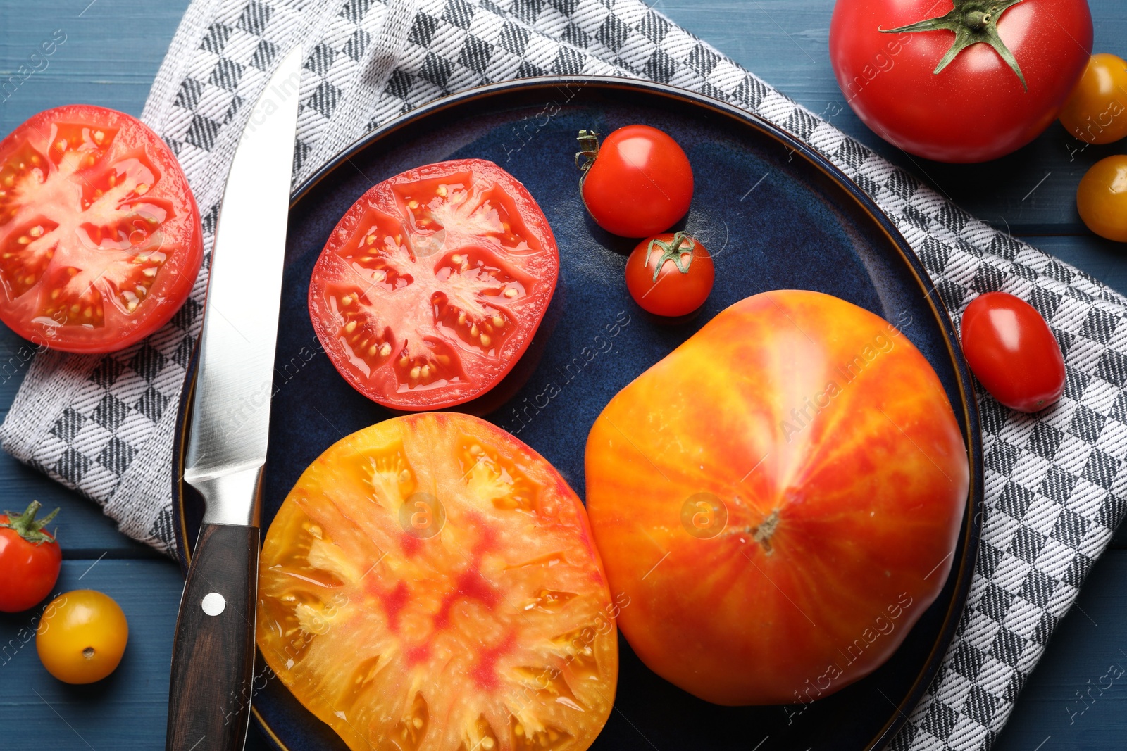 Different ripe tomatoes and knife on blue wooden table, flat lay Photo of Different ripe tomatoes and knife on blue wooden table, flat lay