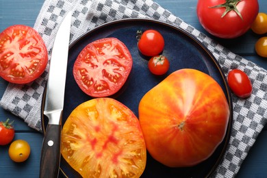 Photo of Different ripe tomatoes and knife on blue wooden table, flat lay