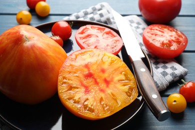 Photo of Different ripe tomatoes and knife on blue wooden table, closeup