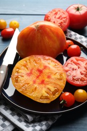 Photo of Different ripe tomatoes and knife on blue wooden table, closeup