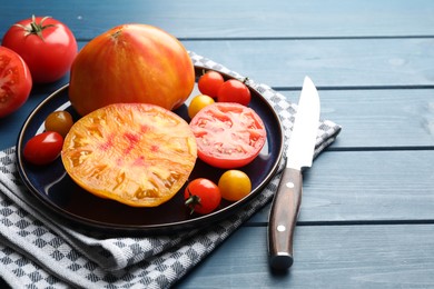 Photo of Different ripe tomatoes and knife on blue wooden table, closeup