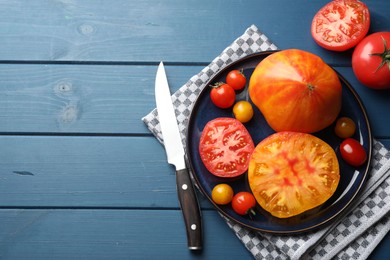 Photo of Different ripe tomatoes and knife on blue wooden table, flat lay. Space for text