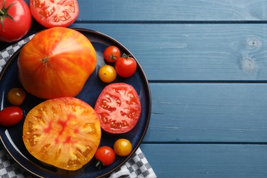 Photo of Different ripe tomatoes on blue wooden table, flat lay. Space for text