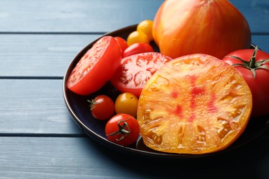 Photo of Different ripe tomatoes on blue wooden table, closeup