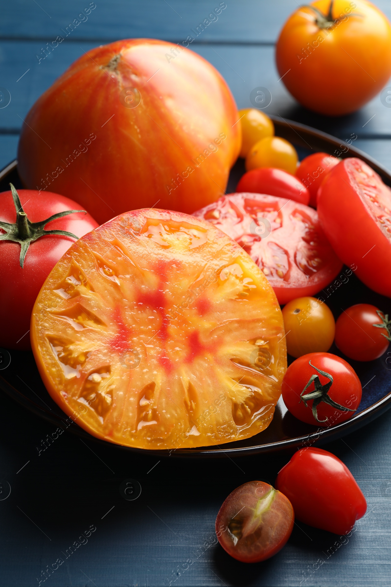 Photo of Different ripe tomatoes on blue wooden table, closeup