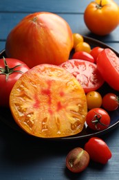 Photo of Different ripe tomatoes on blue wooden table, closeup