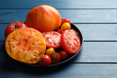 Photo of Different ripe tomatoes on blue wooden table, closeup