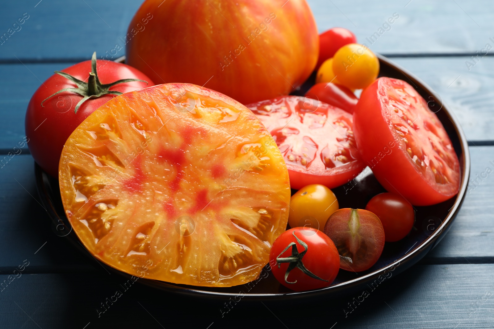 Photo of Different ripe tomatoes on blue wooden table, closeup